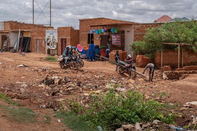 Motorists brave a damaged road in the Kamitete district of Lubumbashi on November 24, 2025. Her parched field is overrun with debris carried by polluted waters, and the little girl in his arms is covered in sores: in Lubumbashi, the mining capital of the DRC, thousands of Congolese claim to be victims of toxic waste from the mining industry. Hélène Mvubu recounts enduring for years the effects of floods caused by contaminated water discharged by Congo Dongfang Mining (CDM), a Chinese mining company that processes copper and cobalt ores in the outskirts of the capital of Katanga province, in the southeastern Democratic Republic of Congo (DRC). (Photo by Glody MURHABAZI / AFP)