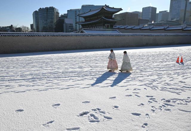 TOPSHOT - Visitors wearing traditional hanbok dresses walk on the snow-covered grounds of Gyeongbokgung Palace in Seoul on December 5, 2025, after the season's first snowfall. (Photo by Jung Yeon-je / AFP)