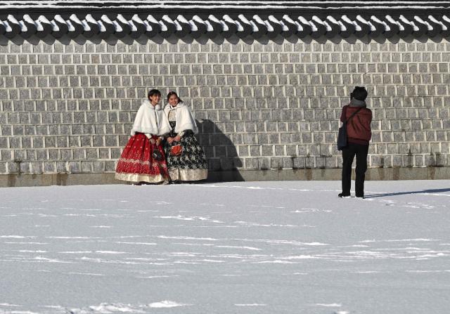 Visitors wearing traditional hanbok dresses pose for photos on the snow-covered grounds of Gyeongbokgung Palace in Seoul on December 5, 2025, after the season's first snowfall. (Photo by Jung Yeon-je / AFP)