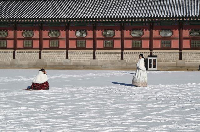 Visitors wearing traditional hanbok dresses pose for photos on the snow-covered grounds of Gyeongbokgung Palace in Seoul on December 5, 2025, after the season's first snowfall. (Photo by Jung Yeon-je / AFP)