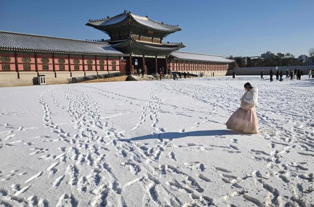 A visitor wearing a traditional hanbok dress walks on the snow-covered grounds of Gyeongbokgung Palace in Seoul on December 5, 2025, after the season's first snowfall. (Photo by Jung Yeon-je / AFP)