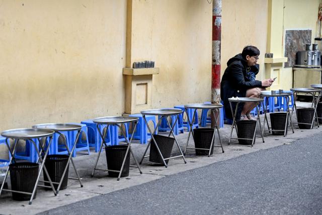 A customer uses her phone as she sits at a roadside restaurant in the Old Quarter of Hanoi on December 5, 2025. (Photo by Nhac NGUYEN / AFP)