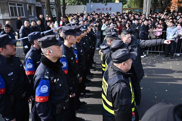 Police officers stand on a street as people wait for the arrival of French President Emmanuel Macron at the University of Sichuan for a meeting with students in Chengdu, in southwestern China's Sichuan province on December 5, 2025. (Photo by Pedro Pardo / AFP)