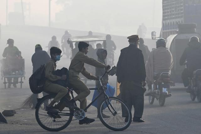 Schoolchildren ride a bicycle along a street on a smoggy morning in Lahore on December 5, 2025. (Photo by Arif ALI / AFP)