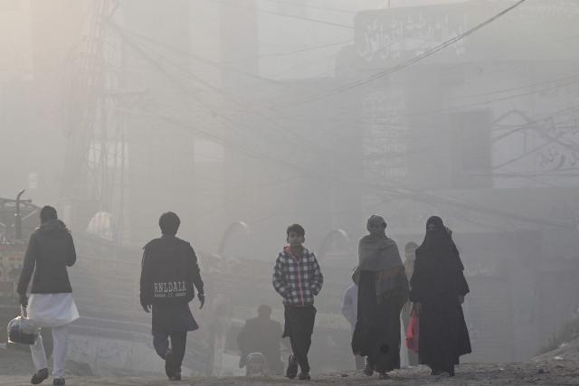 People walk along a street on a smoggy morning in Lahore on December 5, 2025. (Photo by Arif ALI / AFP)