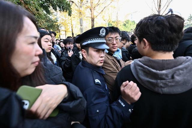 A policeman walks past people waiting for the arrival of French President Emmanuel Macron at the University of Sichuan for a meeting with students in Chengdu, in southwestern China's Sichuan province on December 5, 2025. (Photo by Pedro Pardo / AFP)