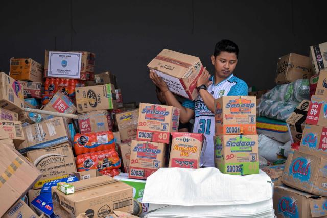 A volunteer packs supplies to be delivered to areas affected by flooding at a Regional Disaster Mitigation Agency in Sidoarjo, East Java province on December 5, 2025. Survivors in Indonesia were piecing back shattered lives December 5 after devastating floods killed more than 1,500 people across four countries, with fears of fresh misery as more rain looms. (Photo by JUNI KRISWANTO / AFP)