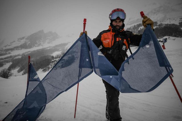 A ski patroller deploys a signage banner on a run during a snowfall at the Gourette ski resort near the Col d'Aubisque pass in the Pyrenees, south-western France on December 2, 2025. The family-oriented resort features one of the largest beginner areas in the Pyrenees and is a pioneer in the mountain range where skiing was first introduced in 1903 near Col d'Aubisque pass. (Photo by Philippe LOPEZ / AFP)