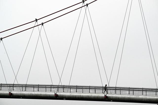 A person crosses the Holbeinsteg pedestrian bridge over the river Main on a cloudy day in Frankfurt am Main, western Germany, on December 5, 2025. (Photo by Kirill KUDRYAVTSEV / AFP)