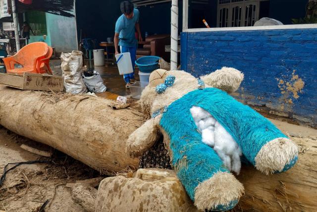 A damage bunny doll is being sun-dried next to a villager affected by flash floods clearing mud from his home in Central Tapanuli, North Sumatra province on December 5, 2025. (Photo by DAMAI MENDROFA / AFP)
