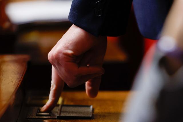 This photograph shows a Member of Parliament taking part in an electronic vote during a voting session focused on the second part of the 2026 social security budget bill (PLFSS) at the National Assembly, the French Parliament lower house, in Paris on December 5, 2025. In a suspenseful vote, the National Assembly narrowly adopted today the "revenue" section of the Social Security budget bill, a crucial vote that allows debates to continue on the expenditure section, particularly regarding the "suspension" of the pension reform. (Photo by Ian LANGSDON / AFP)