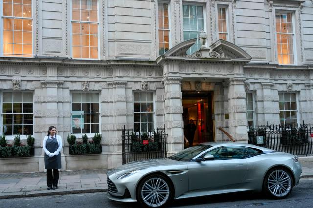 A gallery assistant poses with an Aston Martin DB12 Goldfinger 007 Special Edition car, during a photocall ahead of the "Groundbreakers: Icons of Our Time" auction, at Christie's auctioneers in London on December, 5, 2025. (Photo by CARLOS JASSO / AFP)