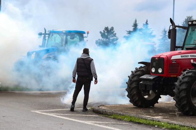 TOPSHOT - A protestor stands amid the smoke from teargas fired by riot police as farmers block the road leading to the airport with their tractors during a protest over the reduced and delayed payment of European Union subsidies, in Thessaloniki on December 5, 2025. (Photo by AFP)