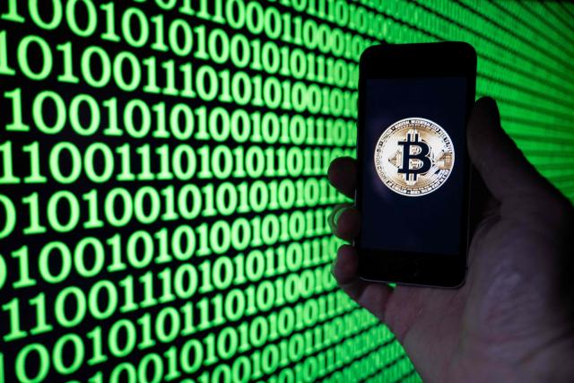 This illustration photograph shows a man holding a phone displaying a Bitcoin logo, in Mulhouse on December 5, 2025. (Photo by SEBASTIEN BOZON / AFP)