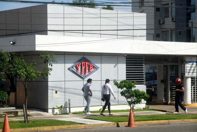 Men walk at the Guillermo Elder Bell refinery headqaurters of Bolivian state-owned oil company YPFB in Santa Cruz, Bolivia, on December 5, 2025. On Tuesday, Bolivia's new centre-right government denounced the misappropriation of millions of dollars worth of fuel under previous administrations of the MOvimiento Al Socialismo (MAS) party, which even impacted the country during the recent fuel shortage crisis. This week, the public prosecutor's office raided the state oil company YPFB and the National Hydrocarbons Agency, which are under investigation for alleged corruption. (Photo by Rodrigo URZAGASTI / AFP)