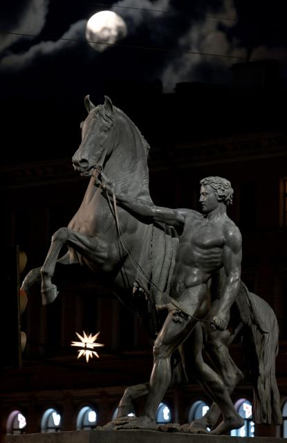 A moon is seen behind the sculpture "Horse with a Walking Youth" created by sculptor Pyotr Klodt, on the Anichkov Bridge in Saint Petersburg on December 5, 2025. (Photo by Olga MALTSEVA / AFP)