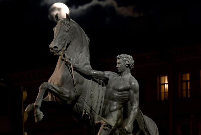 A moon is seen behind the sculpture "Horse with a Walking Youth" created by sculptor Pyotr Klodt, on the Anichkov Bridge in Saint Petersburg on December 5, 2025. (Photo by Olga MALTSEVA / AFP)