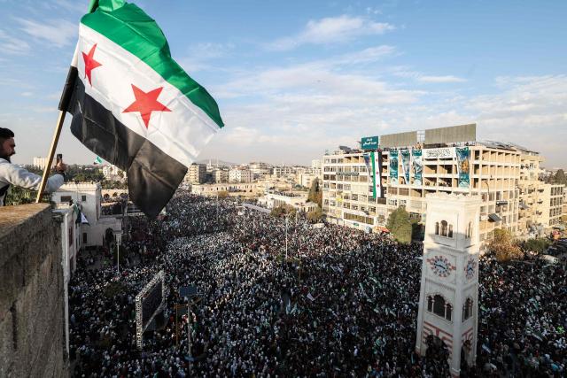 A Syrian flag flutters above crowds gathering during celebrations marking one year since a lightning Islamist-led offensive that eventually toppled the country's longtime ruler, in central Hama on December 5, 2025. (Photo by OMAR HAJ KADOUR / AFP)