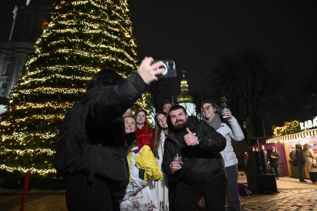 Local residents take a selfie picture during the unveiling ceremony of Kyiv's main Christmas tree on the St. Sophia Square in the Ukrainian capital of Kyiv, on December 5, 2025, amid the Russian invasion of Ukraine. (Photo by Genya SAVILOV / AFP)