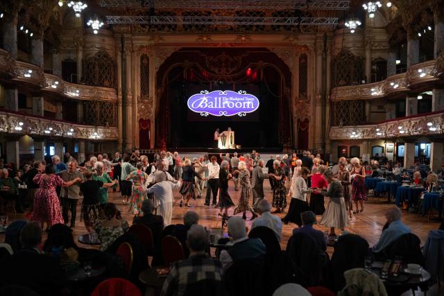 Ballroom dancers take part in a Tea Dance, accompanied by a live organist, in the Blackpool Tower Ballroom, in Blackpool, north west England on October 22, 2025. Tea dances, which evolved from the tradition of afternoon tea in the late 19th century, are enjoying a revival, especially since the pandemic. Often cited as an effective way to combat loneliness, the dances are also attributed to improving the participants' mental and physical health. Frequently hosted in Victorian and Edwardian-era halls, tea dances typically offer a mixture of ballroom and sequence dancing styles and feature refreshments of tea, coffee and cakes. (Photo by Oli SCARFF / AFP)