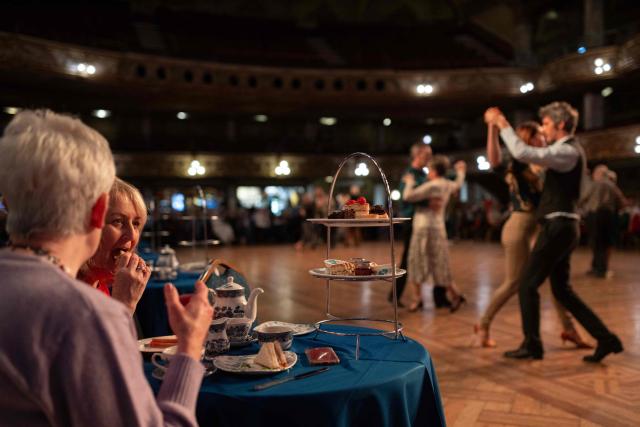 Attendees enjoy afternoon tea and cakes as ballroom dancers take part in a Tea Dance, accompanied by a live organist, in the Blackpool Tower Ballroom, in Blackpool, north west England on October 22, 2025. Tea dances, which evolved from the tradition of afternoon tea in the late 19th century, are enjoying a revival, especially since the pandemic. Often cited as an effective way to combat loneliness, the dances are also attributed to improving the participants' mental and physical health. Frequently hosted in Victorian and Edwardian-era halls, tea dances typically offer a mixture of ballroom and sequence dancing styles and feature refreshments of tea, coffee and cakes. (Photo by Oli SCARFF / AFP)