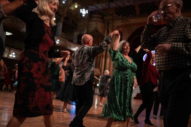 Ballroom dancers take part in a Tea Dance, accompanied by a live organist, in the Blackpool Tower Ballroom, in Blackpool, north west England on October 22, 2025. Tea dances, which evolved from the tradition of afternoon tea in the late 19th century, are enjoying a revival, especially since the pandemic. Often cited as an effective way to combat loneliness, the dances are also attributed to improving the participants' mental and physical health. Frequently hosted in Victorian and Edwardian-era halls, tea dances typically offer a mixture of ballroom and sequence dancing styles and feature refreshments of tea, coffee and cakes. (Photo by Oli SCARFF / AFP)