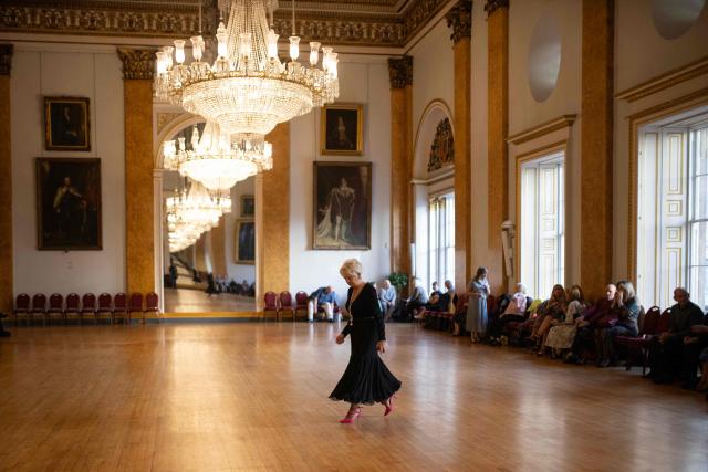A ballroom dancer crosses the dancefloor to speak to a friend before taking part in a Tea Dance, held in the Main Ballroom of Liverpool Town Hall, in Liverpool, north west England on November 17, 2025. Tea dances, which evolved from the tradition of afternoon tea in the late 19th century, are enjoying a revival, especially since the pandemic. Often cited as an effective way to combat loneliness, the dances are also attributed to improving the participants' mental and physical health. Frequently hosted in Victorian and Edwardian-era halls, tea dances typically offer a mixture of ballroom and sequence dancing styles and feature refreshments of tea, coffee and cakes. (Photo by Oli SCARFF / AFP)