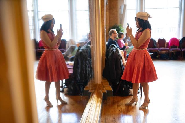 A ballroom dancer records herself in a large mirror during a Tea Dance, held in the Main Ballroom of Liverpool Town Hall, in Liverpool, north west England on November 17, 2025. Tea dances, which evolved from the tradition of afternoon tea in the late 19th century, are enjoying a revival, especially since the pandemic. Often cited as an effective way to combat loneliness, the dances are also attributed to improving the participants' mental and physical health. Frequently hosted in Victorian and Edwardian-era halls, tea dances typically offer a mixture of ballroom and sequence dancing styles and feature refreshments of tea, coffee and cakes. (Photo by Oli SCARFF / AFP)