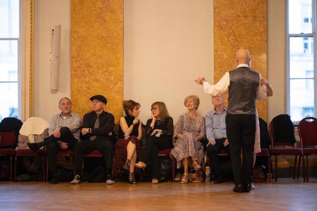 Ballroom dancers sit as they take a break from dancing during a Tea Dance, in the Main Ballroom of Liverpool Town Hall, in Liverpool, north west England on November 17, 2025. Tea dances, which evolved from the tradition of afternoon tea in the late 19th century, are enjoying a revival, especially since the pandemic. Often cited as an effective way to combat loneliness, the dances are also attributed to improving the participants' mental and physical health. Frequently hosted in Victorian and Edwardian-era halls, tea dances typically offer a mixture of ballroom and sequence dancing styles and feature refreshments of tea, coffee and cakes. (Photo by Oli SCARFF / AFP)