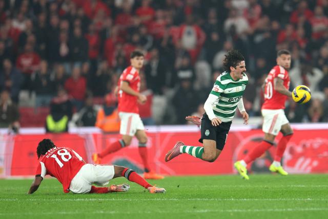 Sporting Lisbon's Portuguese forward #17 Francisco Trincao falls as he fights for the ball with SL Benfica's Luxembourgish midfielder #18 Leandro Barreiro during the Portuguese League football match between SL Benfica and Sporting CP at Estadio da Luz in Lisbon on December 5, 2025. (Photo by PATRICIA DE MELO MOREIRA / AFP)