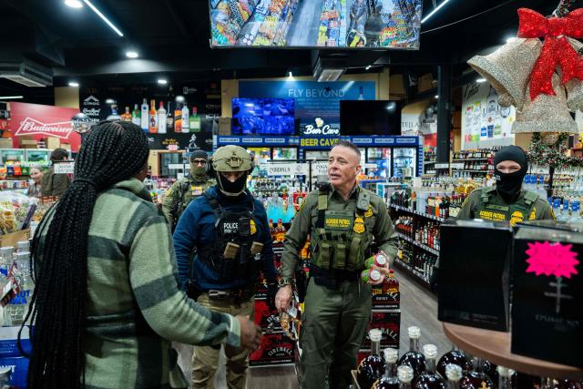 US Customs and Border Patrol Commander Gregory Bovino (C-R) speaks to a customer while buying snacks at a gas station convenience store during an immigration raid in Kenner, Louisiana, on December 5, 2025. The US Department of Homeland Security announced on December 3 it has launched a federal immigration enforcement operation, named "Operation Catahoula Crunch," in the New Orleans, Louisiana, area. (Photo by Adam GRAY / AFP)