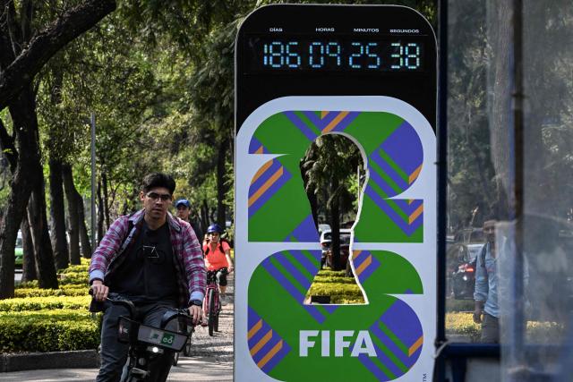 A cyclist rides past a countdown to the 2026 FIFA World Cup inaugural match between Mexico and South Africa in Mexico City on December 5, 2025. The draw for the 2026 World Cup, held this Friday in Washington, shaped an unprecedented group stage: 48 teams distributed into 12 groups of four teams each, with the hosts United States, Mexico and Canada seeded in Groups D, A and B, respectively. (Photo by Yuri CORTEZ / AFP)
