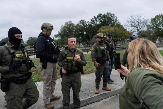 An activist films with her mobile phone as US Customs and Border Patrol Commander Gregory Bovino (3-L) leads his agents to interview people at a park in Metairie, Louisiana, on December 5, 2025. The US Department of Homeland Security announced on December 3 it has launched a federal immigration enforcement operation, named "Operation Catahoula Crunch," in the New Orleans, Louisiana, area. (Photo by Adam GRAY / AFP)