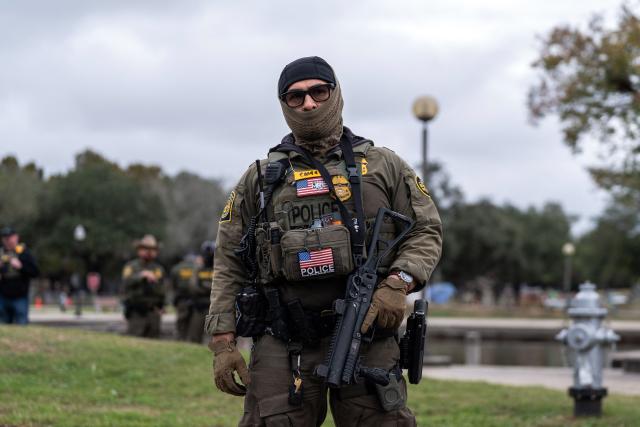 A US Customs and Border Patrol agent stands guard as Commander Gregory Bovino conducts interviews with residents during operations at a park in Metairie, Louisiana, on December 5, 2025. The US Department of Homeland Security announced on December 3 it has launched a federal immigration enforcement operation, named "Operation Catahoula Crunch," in the New Orleans, Louisiana, area. (Photo by Adam GRAY / AFP)