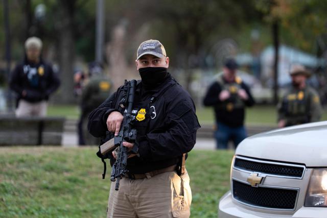 A US Customs and Border Patrol agent stands guard as Commander Gregory Bovino conducts interviews with residents during operations at a park in Metairie, Louisiana, on December 5, 2025. The US Department of Homeland Security announced on December 3 it has launched a federal immigration enforcement operation, named "Operation Catahoula Crunch," in the New Orleans, Louisiana, area. (Photo by Adam GRAY / AFP)