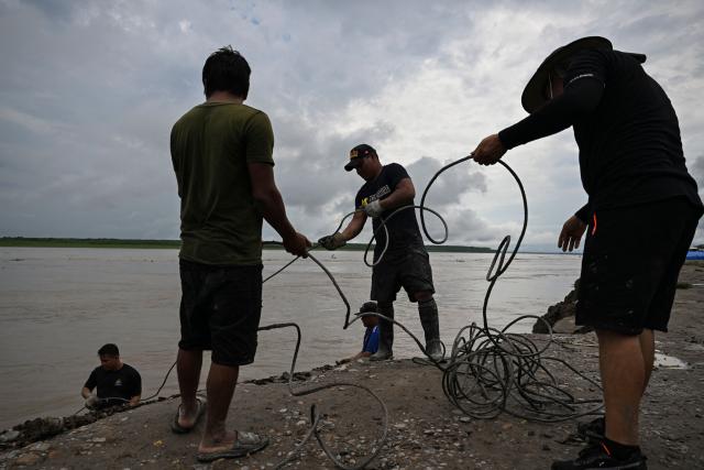 Police officers of a rescue team work on the area of a vessel accident at the port of Iparia, in the Ucayali department in Peru's central jungle, on December 5, 2025. At least 12 people, including three children, died on December 1, 2025, when a landslide buried two boats docked at a river port in central Peru, with dozens of others missing, officials said. (Photo by Hugo Alejos / AFP)