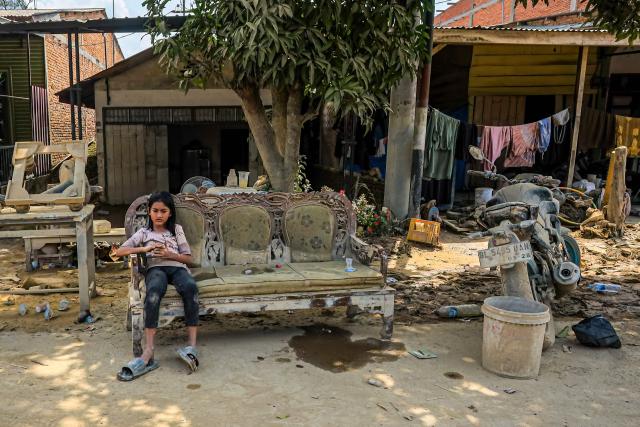 This picture taken on December 5, 2025 shows a young girl sitting on a mud-stained sofa among belongings in a flood affected area in Aceh Tamiang, Aceh province. Survivors in Indonesia were piecing back shattered lives on December 5 after devastating floods killed more than 1,750 people across five countries, with fears of fresh misery as more rain looms. (Photo by AMANDA JUFRIAN / AFP)