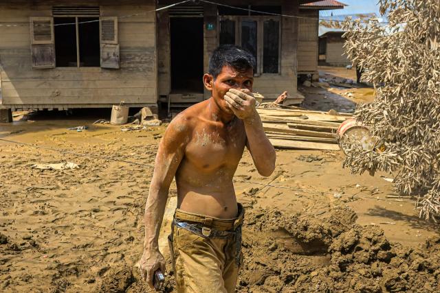 TOPSHOT - This picture taken on December 5, 2025 shows a man covered with mud in front of a house in a flood affected area in Aceh Tamiang, Aceh province. Survivors in Indonesia were piecing back shattered lives on December 5 after devastating floods killed more than 1,750 people across five countries, with fears of fresh misery as more rain looms. (Photo by AMANDA JUFRIAN / AFP)