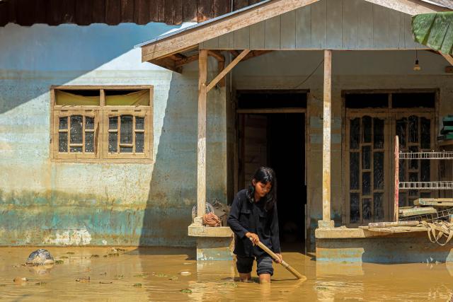 This picture taken on December 5, 2025 shows a young girl walking through mud in front of her house in a flood affected area in Aceh Tamiang, Aceh province. Survivors in Indonesia were piecing back shattered lives on December 5 after devastating floods killed more than 1,750 people across five countries, with fears of fresh misery as more rain looms. (Photo by AMANDA JUFRIAN / AFP)