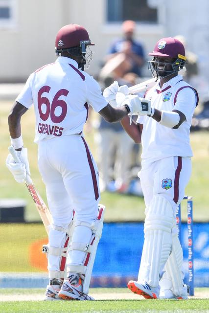 West Indies' Kemar Roach (R) is congratulated by Justin Greaves after he scored his half century during day five of the first Test cricket match between New Zealand and West Indies at Hagley Oval in Christchurch on December 6, 2025. (Photo by Sanka Vidanagama / AFP)