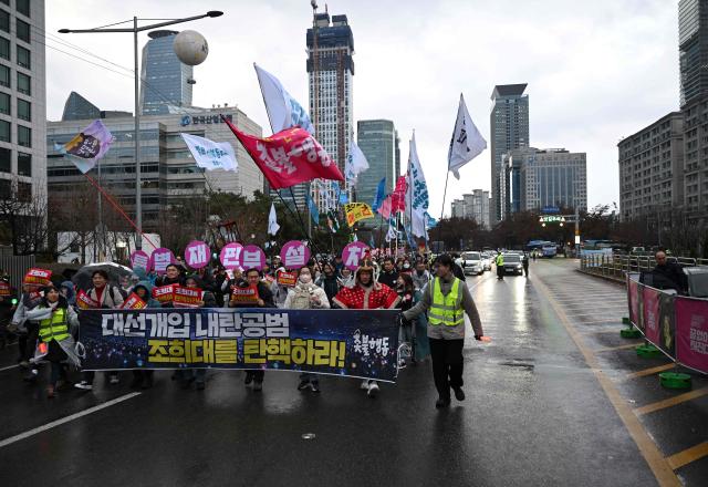Protesters carry a banner reading "Impeach Cho Hee-dae, Chief Justice of the Supreme Court of South Korea, for complicity in insurrection!" as they march during a rally marking the first anniversary of South Korean ousted president Yoon Suk Yeol's declaration of martial law, near the National Assembly in Seoul on December 6, 2025. (Photo by Jung Yeon-je / AFP)