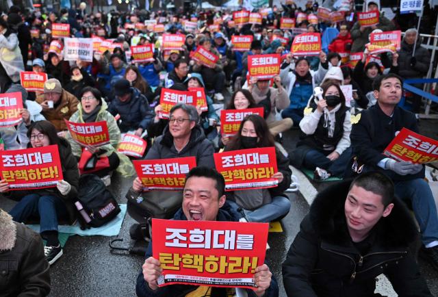 Protesters hold placards reading "Impeach Cho Hee-dae, the Chief Justice of the Supreme Court of South Korea!" during a rally marking the first anniversary of South Korean ousted president Yoon Suk Yeol's declaration of martial law, near the National Assembly in Seoul on December 6, 2025. (Photo by Jung Yeon-je / AFP)