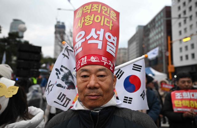 A protester holds a placard above his head that reads "Execute Yoon Suk Yeol who is a high-ranking criminal!" during a rally marking the first anniversary of South Korean ousted president Yoon Suk Yeol's declaration of martial law, near the National Assembly in Seoul on December 6, 2025. (Photo by Jung Yeon-je / AFP)