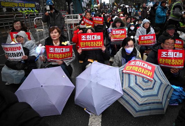 Protesters hold placards reading "Impeach Cho Hee-dae, the Chief Justice of the Supreme Court of South Korea!" during a rally marking the first anniversary of South Korean ousted president Yoon Suk Yeol's declaration of martial law, near the National Assembly in Seoul on December 6, 2025. (Photo by Jung Yeon-je / AFP)