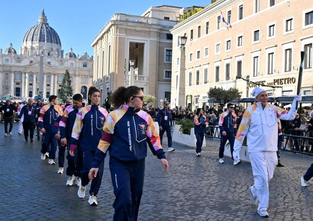 A torchbearer carries the Olympic torch along the Via della Conciliazione as Saint Peter's Basilica in the background during the Torch Relay to Milano Cortina 2026 Olympic Games, in Rome on December 6, 2025. (Photo by Filippo MONTEFORTE / AFP)