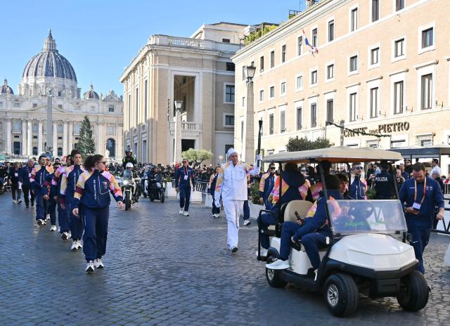 A torchbearer carries the Olympic torch along the Via della Conciliazione as Saint Peter's Basilica in the background during the Torch Relay to Milano Cortina 2026 Olympic Games, in Rome on December 6, 2025. (Photo by Filippo MONTEFORTE / AFP)