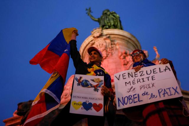 Attendees hold placards including one (L) reading "Venezeula deserves the Nobel Peace Prize" as they take part in a demonstration organised by the Venezuelan political opposition, at place de la Republique, with the Monument a la Republique statue in the background, in Paris on December 6, 2025. The Venezuelan opposition called on December 5 for marches in several cities around the world, on December 6 in Oslo, four days before the Nobel Peace Prize ceremony, honoring laureate Maria Corina Machado, whose attendance remains uncertain. The leader of the Venezuelan opposition has been living in hiding since August 2024 following the contestation of the July 28 presidential election, but she has expressed her intention to attend the ceremony on December 10. (Photo by Ian LANGSDON / AFP)