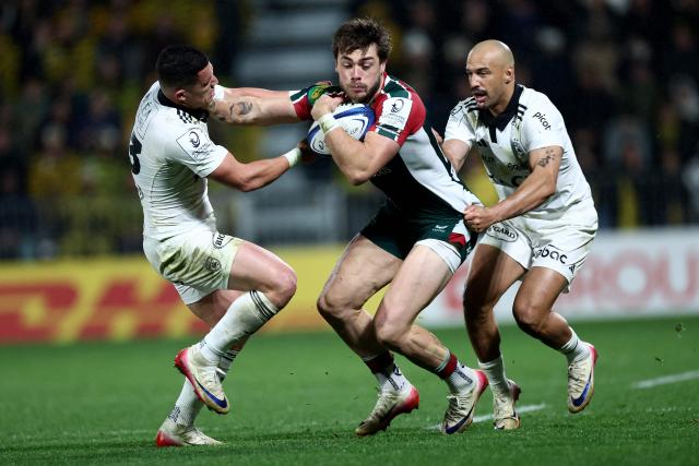 Leicester's English wing Ollie Hassell-Collins (C) is tackled by La Rochelle' French centre Adrien Seguret (L) and La Rochelle's South African fullback Dillyn Leyds (R) during the European Rugby Champions Cup rugby union match between Stade Rochelais (La Rochelle) and Leicester Tigers at the Marcel-Deflandre Stadium in La Rochelle, western France on December 6, 2025. (Photo by ROMAIN PERROCHEAU / AFP)