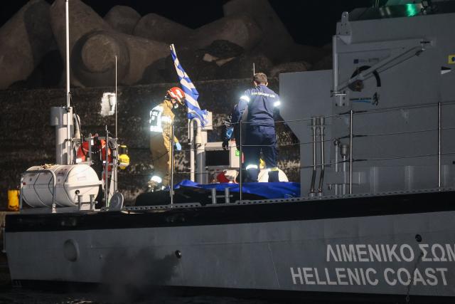Firefighters and members of the Hellenic coast guards stand next to bags with bodies in a coast guard vessel after a migrant vessel sank off, at the port in Ierapetra on Island of Crete, on December 6, 2025. Seventeen men were found dead Saturday after a migrant vessel sank off the Greek island of Crete, a coastguard spokeswoman told AFP. "Two survivors in a critical condition have been hospitalised," the spokeswoman added. (Photo by Costas METAXAKIS / AFP)