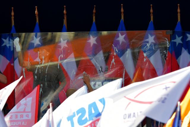 Workers clean the bulletproof glass protecting Chilean presidential candidate Jose Antonio Kast of the Republican Party before his closing campaign rally in Concepcion, Chile, on December 6, 2025. Chile will choose its next president in a runoff on December 14, with far-right candidate Jose Antonio Kast as the clear favorite against leftist Jeannette Jara, after a campaign marked by fears over crime and irregular migrants. (Photo by GUILLERMO SALGADO / AFP)